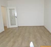 Ein Zimmer in einer 3-Zimmer-Wohnung mit weißen Wänden und einem Boden in Holzoptik.