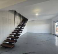 Innenraum der Villa mit Metalltreppe und Holzboden, großes Fenster zur Terrasse.