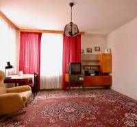 Wohnzimmer in einem Einfamilienhaus mit rotem Teppich, Sessel und Vorhängen an den Fenstern.