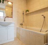 Badezimmer in einer 2-Zimmer-Wohnung mit Badewanne, Waschbecken, Spiegel und beigen Fliesen.