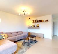 Wohnzimmer in einem Einfamilienhaus mit einer Eckcouch, runden Tischen und einem Boden in Holzoptik.