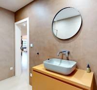 Badezimmer in einem Einfamilienhaus mit Waschbecken, rundem Spiegel und Duschkabine.