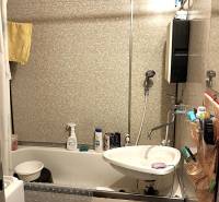 Badezimmer in einer 2-Zimmer-Wohnung mit Badewanne, Waschbecken und gefliesten Wänden.