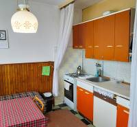 Küche mit älteren Möbeln in einer 2-Zimmer-Wohnung, orangefarbene Schränke, Tisch, Kronleuchter.