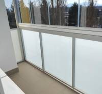 Ein verglaster Balkon in einer 2-Zimmer-Wohnung mit Blick auf Bäume und Berge.