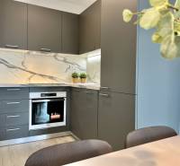 Küche in einer 2-Zimmer-Wohnung mit Steinverkleidung und grauen Schränken.