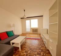 Wohnzimmer in einer 2-Zimmer-Wohnung mit einem Sofa, weißen Möbeln, bunten Kissen und einem Boden in Holzoptik.