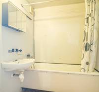 Badezimmer mit Badewanne und Duschvorhang in einer 2-Zimmer-Wohnung, helle Wände, orangener Boden.