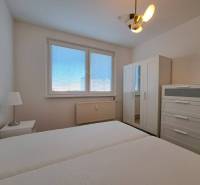 Schlafzimmer in einer 2-Zimmer-Wohnung mit weißen Möbeln und Bett, Fenster mit Jalousien.