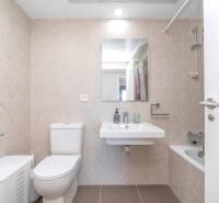 Badezimmer in einer 2-Zimmer-Wohnung mit Toilette, Waschbecken, Badewanne und beigen Fliesen.