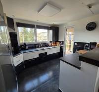 Eine Küche in einem Einfamilienhaus mit Keramikboden, dunklen Möbeln und großen Fenstern.