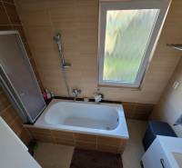 Ein Badezimmer in einem Einfamilienhaus mit einer Badewanne und einem Fenster, gefliest mit braunen Fliesen.