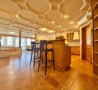 Innenraum einer 4-Zimmer-Wohnung mit dekorativer Decke, Holzboden, Kücheninsel und Stühlen.