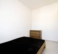 Schlafzimmer in einer 2-Zimmer-Wohnung, enthält ein Bett, eine Kommode und einen Boden mit Holzdekor.