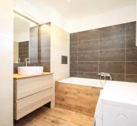 Ein Badezimmer mit hellen Fliesen, einer Waschmaschine und einem Boden mit Holzdekor in einer 2-Zimmer-Wohnung.