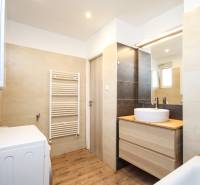 Badezimmer in einer 2-Zimmer-Wohnung mit Waschbecken, Spiegel, Waschmaschine und Boden mit Holzdekor.