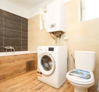 Badezimmer in einer 2-Zimmer-Wohnung mit Holzboden, Waschmaschine, Badewanne, Boiler.