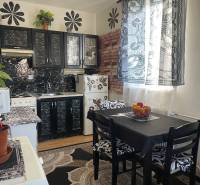 Küche mit Tischen, schwarzen Schränken und gemusterten Vorhängen in einer Einzimmerwohnung.