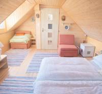 Ein hölzernes Interieur einer Hütte mit einem Boden in Holzoptik, einem Bett und einem Sessel.