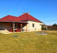 Ein Einfamilienhaus in Zemianska Olča mit rotem Dach und Holzunterstand, grasbewachsener Garten.