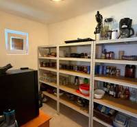 Komora v rodinnom dome s policami plnými zásob a kuchynských spotrebičov.