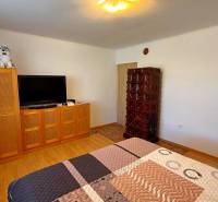 Ein Zimmer in einem Einfamilienhaus mit einem Fernseher, einem Schrank, einem Kachelofen und einem Boden mit Holzdekor.