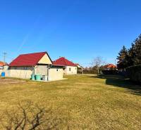 Eine Rasenfläche bei einem Einfamilienhaus in Zemianska Olča mit mehreren Häusern und Sträuchern.