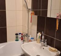 Badezimmer mit Dusche, Waschbecken und Schrank in einer 4-Zimmer-Wohnung, überwiegend dunkle Fliesen.