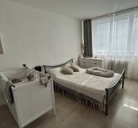 Schlafzimmer in einer 2-Zimmer-Wohnung mit Kinderbett, Bett und Kommode, Boden mit Holzdekor.