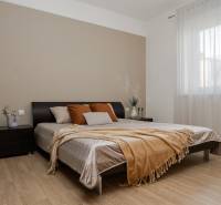 Schlafzimmer in einer 2-Zimmer-Wohnung mit Holzboden, großem Bett und Fenster mit zartem Vorhang.