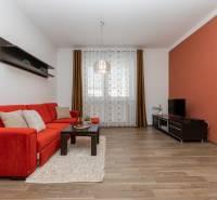 Wohnzimmer mit orangem Sofa, Regalen und Holzboden in einer Zweizimmerwohnung.