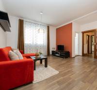 Wohnzimmer in einer 2-Zimmer-Wohnung mit Sofa, Fernseher, Holzboden und dekorativen Vorhängen.