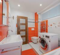Orange-weißes Badezimmer in einer 2-Zimmer-Wohnung mit Waschmaschine und Waschbecken.