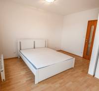 Schlafzimmer in einer 2-Zimmer-Wohnung mit einem weißen Bett und einem Boden in Holzoptik.