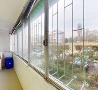 Veranda einer 2-Zimmer-Wohnung mit Plastikstühlen und Blick auf den Parkplatz.