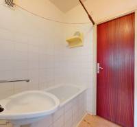 Badezimmer mit weißen Fliesen, Badewanne und Holztür in einer Zweizimmerwohnung.