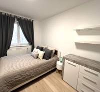 Schlafzimmer in einer 2-Zimmer-Wohnung mit Bett, Kommode und Vorhängen, Boden mit Holzdekor.