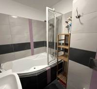Badezimmer in einer 2-Zimmer-Wohnung mit Eckbadewanne, Fliesen und Handtuchhalter.