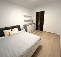 Schlafzimmer mit grauem Bett, Schrank und Boden mit Holzdekor in einer 2-Zimmer-Wohnung.