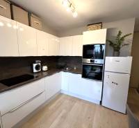 Küche in einer 2-Zimmer-Wohnung mit weißen Schränken, Geräten und einem Boden in Holzoptik.