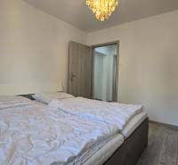 Schlafzimmer in einer 2-Zimmer-Wohnung mit Doppelbett, heller Wand und Boden in Holzoptik.