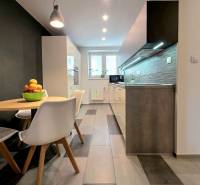 Küche in einer 2-Zimmer-Wohnung mit Esstisch, Fliesenboden und Leuchten über der Arbeitsplatte.