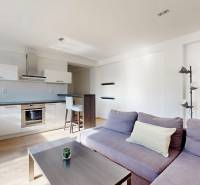 Wohnzimmer mit Küche, lila Sofa, weiße Küchenzeile, Boden mit Holzdekor.