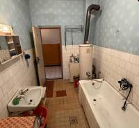 Das Badezimmer in einem Einfamilienhaus enthält eine Badewanne, ein Waschbecken, alte Möbel und einen Boiler.