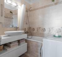 Badezimmer in einer 4-Zimmer-Wohnung mit Badewanne, Waschbecken, Waschmaschine und dekorativen Blumen.