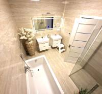 Badezimmer in einem Einfamilienhaus mit Badewanne, Waschbecken, Blumengesteck und großem Spiegel.