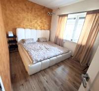 Ein Schlafzimmer in einem Einfamilienhaus mit einem Bett, einem Boden in Holzoptik und einer goldenen Wand.