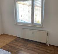 Weiße Wand, Fenster mit Jalousien, Boden mit Holzdekor, Heizkörper in einer 3-Zimmer-Wohnung.