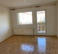 Ein Zimmer in einer 3-Zimmer-Wohnung mit Holzboden und Zugang zum Balkon.