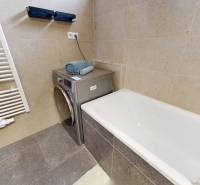 Badezimmer in einer 3-Zimmer-Wohnung mit Badewanne, Waschmaschine und Handtüchern auf beigen Fliesen.